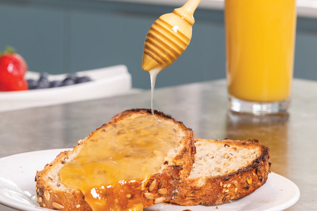 Argan Honey being drizzled onto toast with a glass of orange juice in the background.
