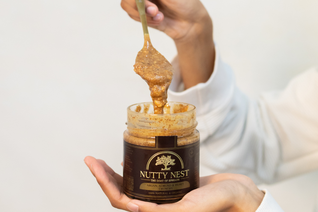 Close-up of NuttyNest crunchy almond butter with argan oil and honey on a spoon, showing creamy texture with crunchy almond pieces.